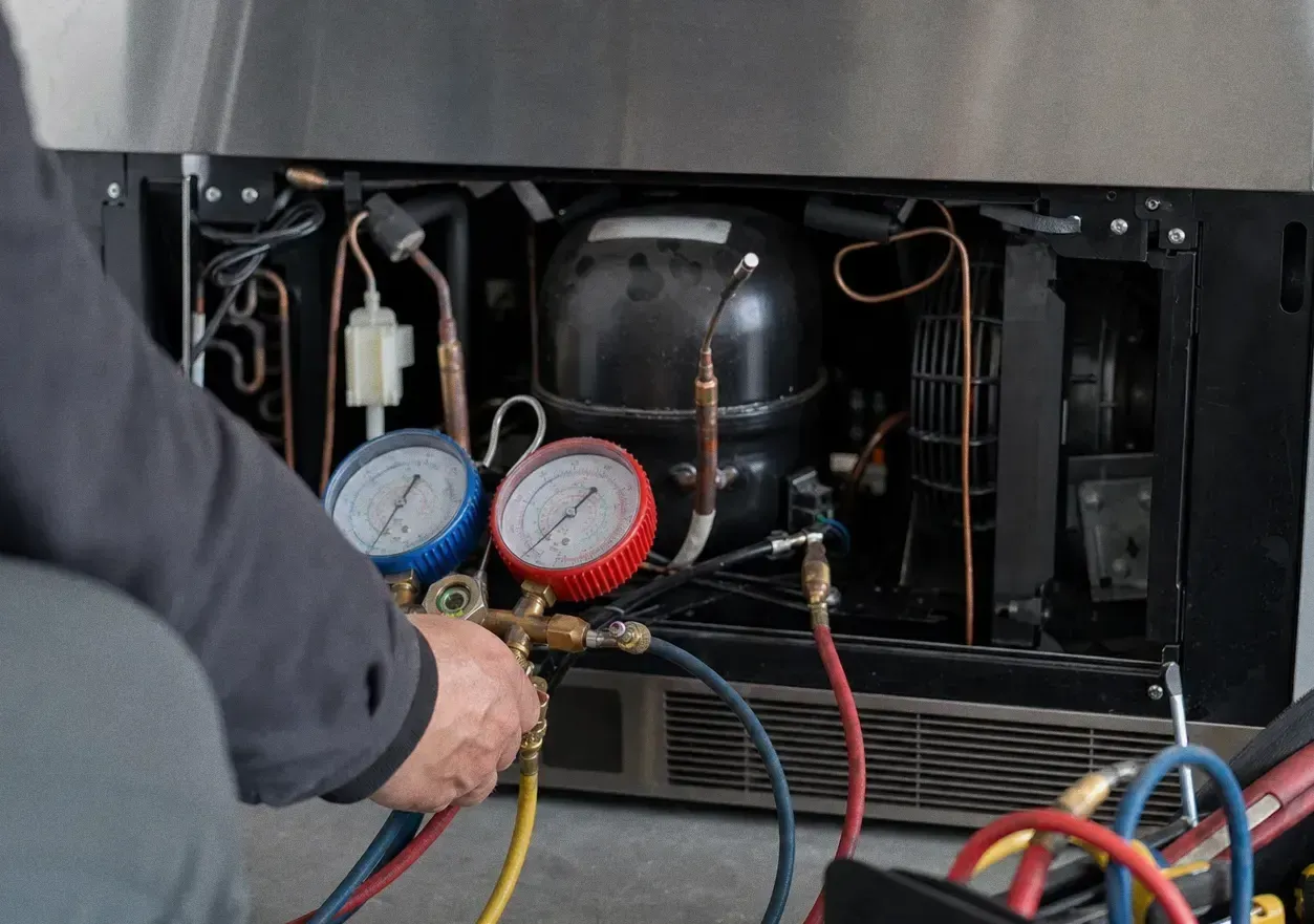 Refrigerant manifold gauges with red and blue hoses connected to the compressor compartment of a built-in refrigerator