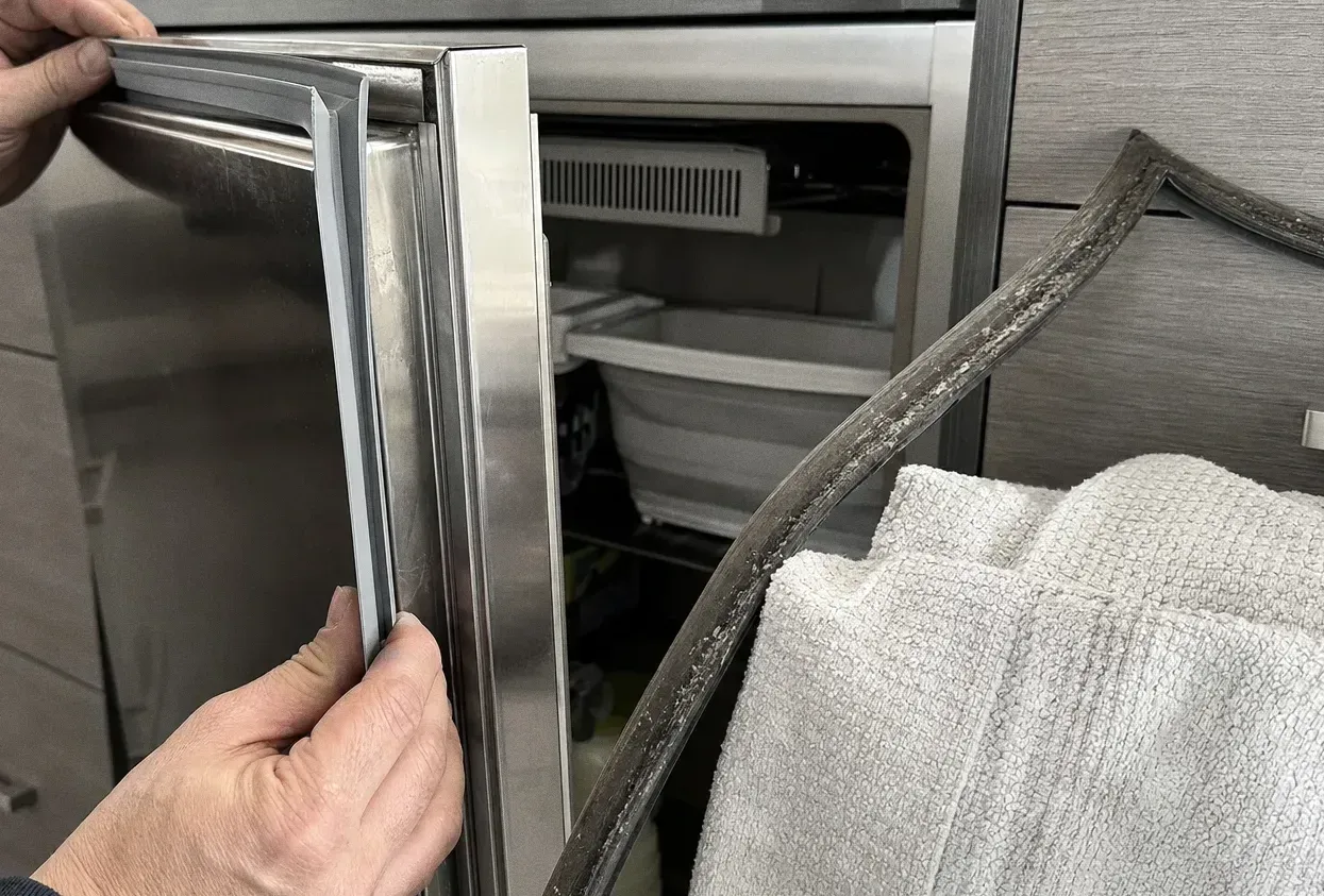 A stainless appliance door held open by its edge, gasket visible along the frame and a freezer drawer behind it